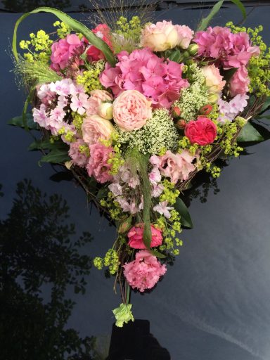 Bunte Blumenanordnung in Herzform auf schwarzem Untergrund.