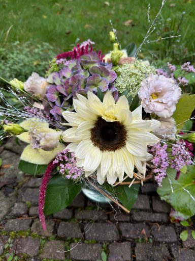 Bunte Blumenarrangement mit Sonnenblume, Orchideen und verschiedenen grünen Blättern.