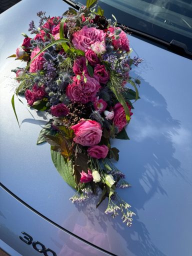 Bunte Blumenarrangement auf einer silbernen Autokapote.