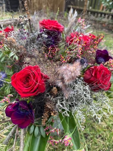 Bunte Blumenarrangement mit roten Rosen, lila Blüten und dekorativen Trockenblumen.