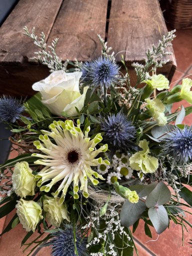 Bunte Blumenarrangement mit weißen und blauen Blüten sowie grünen Akzenten.